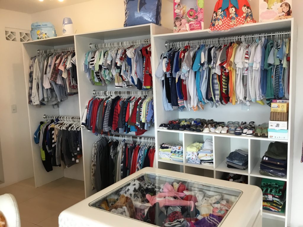 Araras de roupas infantis, prateleiras com calçados e balcão de acessórios no interior da loja.