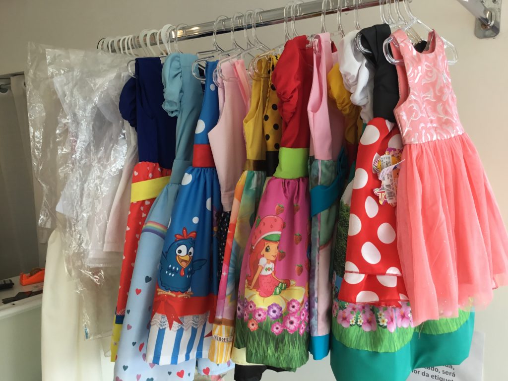 Vestidos infantis coloridos e estampados pendurados em uma arara.